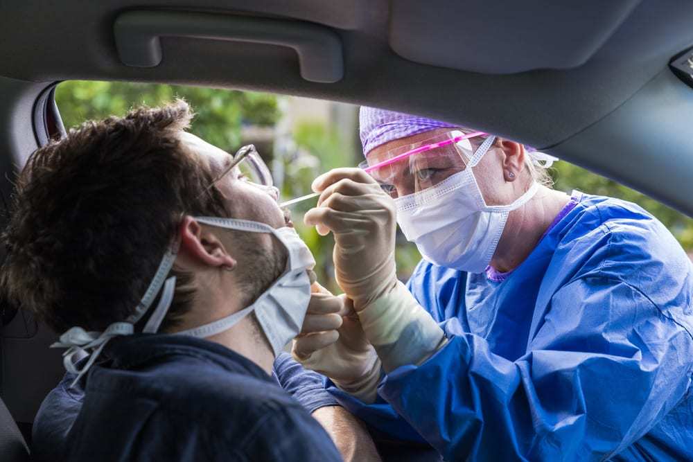 Health care worker in protective gear taking a nasal swab of a man in a car