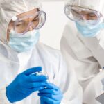 Two scientists in PPE examine vaccine, write on clipboard
