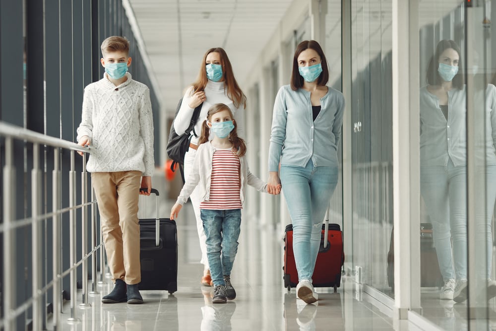 Family wearing face masks at the airport, rolling luggage