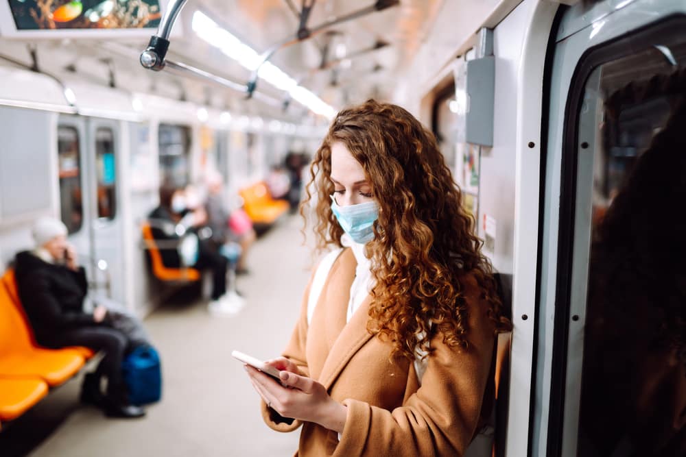 Young-woman-wearing-mask-on-subway-and-looking-at-phone